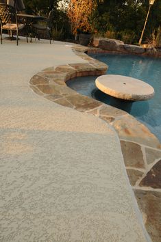 an outdoor swimming pool with stone steps leading up to it and chairs in the background