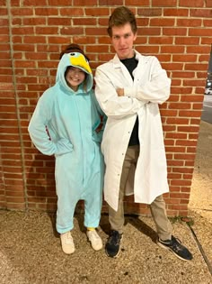 two people in costumes standing next to each other near a brick wall and one is wearing a duck costume