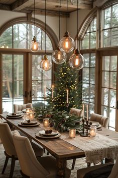 a dining room table with candles and christmas tree in the center, surrounded by large windows