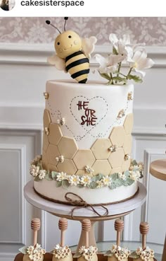 a three tiered cake decorated with flowers and a bee on top is sitting on a table