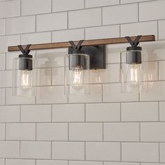 three light fixtures mounted on a white brick wall in a bathroom with wood beam and glass shades