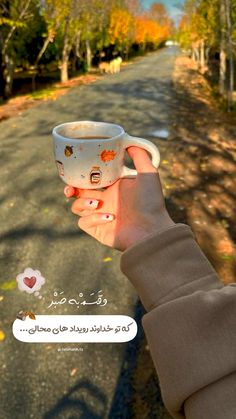 a person holding a cup in the middle of a road with trees and leaves on it