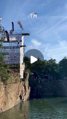 people are flying kites on the edge of a cliff over water with trees and buildings in the background