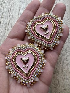 two pink and gold heart shaped brooches on a person's palm hand