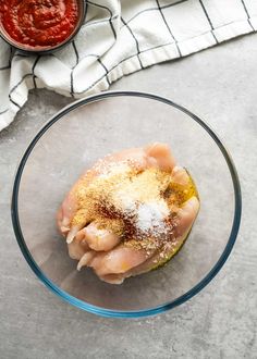 a glass bowl filled with meat and seasoning on top of a counter next to a towel