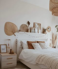 a white bed sitting next to a wall with pictures on top of it and plants in the corner