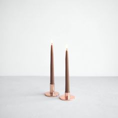 two candles sitting on top of each other in front of a white wall and floor