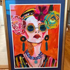 an art piece is displayed on the floor in front of a wooden frame with a painting of a woman wearing sunglasses and flowered headpieces