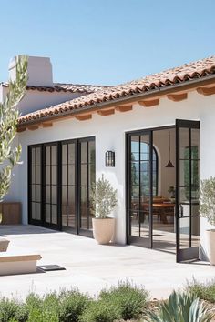 a white house with black glass doors and potted plants on the front patio area