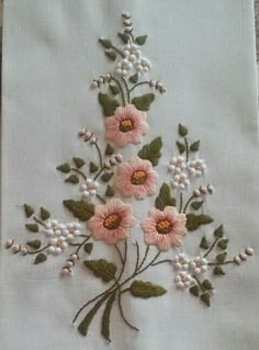 an embroidered piece of cloth with pink flowers and green leaves on the side, sitting on a table