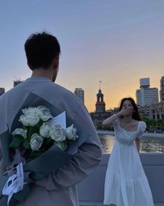 a man and woman standing next to each other on a bridge with the city in the background