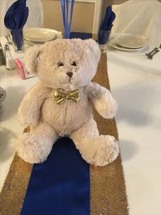 a white teddy bear sitting on top of a blue and gold table runner at a wedding