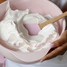 a person holding a pink bowl filled with whipped cream and a wooden spoon in it