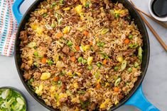 a skillet filled with rice and vegetables on top of a table next to chopsticks