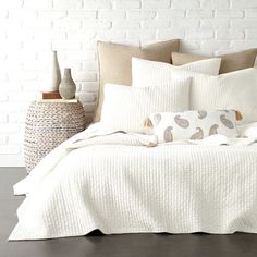 a bed with white sheets and pillows next to a basket filled with vases on top of it