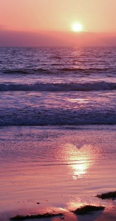 the sun is setting over the ocean with waves coming in and one person walking on the beach