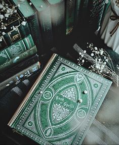 a green book sitting on top of a table next to some flowers and bookshelves