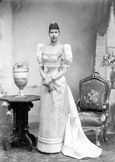 an old black and white photo of a woman standing next to a table with a vase on it