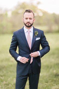 a man wearing a suit and tie standing in the grass with his hands on his hips