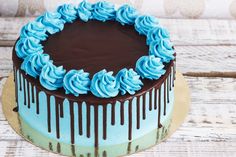 a chocolate cake with blue frosting and drizzled on top sitting on a wooden table