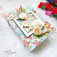 a small album with flowers on it sitting on a white furnishing next to red and pink roses