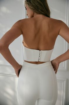 High-end crepe and couture construction make this V-neck crop top perfect for trendy, fashion-loving brides who want to show off their figure. A dainty illusion panel and bridal buttons make this strapless top extra special, while strategically placed seams are sewn to follow your natural curves. Chic Cropped Crop Top For Wedding, Elegant Cropped Crop Top For Wedding, White Crop Top With Corset Back For Party, Elegant Fitted Crop Top With Corset Back, Chic Sleeveless Wedding Crop Top, Elegant Sleeveless Crop Top For Wedding, Elegant Cropped Corset With Boned Bodice, Elegant Evening Corset With Removable Bra Pads, Elegant White Crop Top With Corset Back