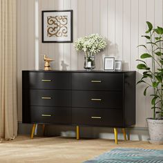 a black dresser with gold handles and drawers in a room next to a potted plant