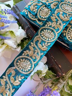 two blue sashes with gold embellishments sit on a table next to flowers