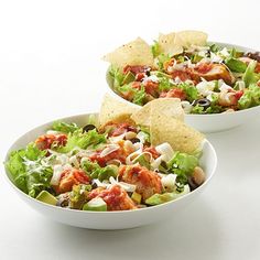 two bowls filled with salad and tortilla chips on top of a white table