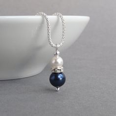 "Simple and elegant in design, this navy pearl necklace would be ideal for bridesmaids or as a \"something blue\" token for a bride. A single white pearl sits in a crystallized band above a lone dark blue pearl. This glass pearl and crystal drop hangs from a Sterling silver corb chain. The lustre of the pearls combined with the sparkle of the crystals make this dark blue pearl necklace ideal for weddings and special occasions .  The 18 inch corb chain is a more ornate alternative to the standard Blue Pearl Drop Necklaces For Wedding, Blue Pearl Chain Jewelry For Wedding, Blue Pearl Drop Necklace For Wedding, Formal Blue Pearl Drop Necklace, Blue Pearl Pendant Jewelry For Wedding, Blue Pearl Chain Necklaces For Wedding, Blue Pearl Chain Necklace For Wedding, Blue Pearl Necklace For Formal Occasions, Formal Blue Pearl Necklace