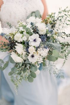 a bride holding a bouquet of white and blue flowers with greenery in her hands