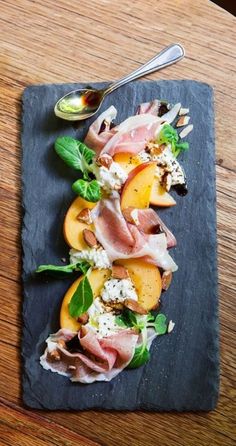 an appetizer with peaches, prosciutto and cheese on a slate platter