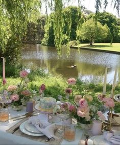 a table set up with flowers and candles for an outdoor dinner by the lake in summer