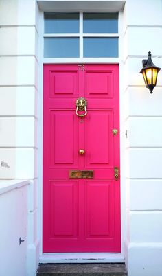 a bright pink door in front of a white house with a lamp on the side