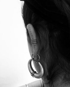 a woman with piercings on her ear and behind her ear is a pair of hoop earrings