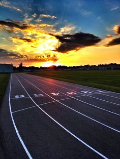 the sun is setting over a running track in an open field with white lines on it