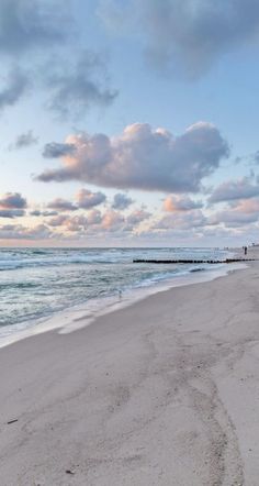 a sandy beach with waves coming in to the shore and clouds over the water at sunset