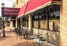 tables and chairs line the outside of an italian restaurant in front of a red awning