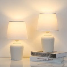 two white lamps sitting next to each other on top of a table with some books