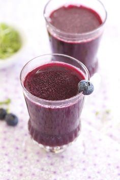 two glasses filled with blueberry smoothie on top of a table