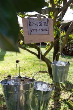 three metal buckets filled with ice sitting on top of a grass covered field next to a tree