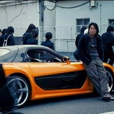 a man standing next to an orange sports car