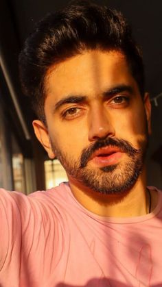 a close up of a person wearing a pink shirt and holding a cell phone in his hand