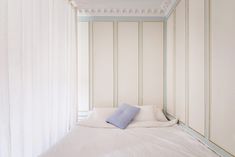 a bed with white sheets and blue pillows in a room that has vertical striped walls