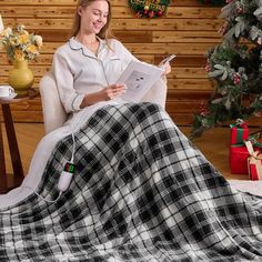 a woman sitting in a chair with a plaid blanket on her lap reading a magazine