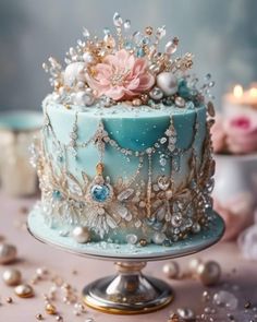 there is a blue cake with pearls and flowers on the top, sitting on a table