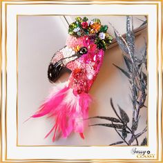 there is a pink bird with feathers and beads on it's head, sitting next to some plants