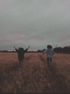 two people are running through a field with their arms in the air and one person is flying a kite