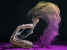 a woman kneeling on the ground with her hair blowing in the wind and dust behind her