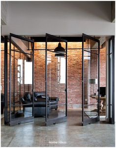 an open room with glass walls and black leather furniture in the corner, next to a brick wall